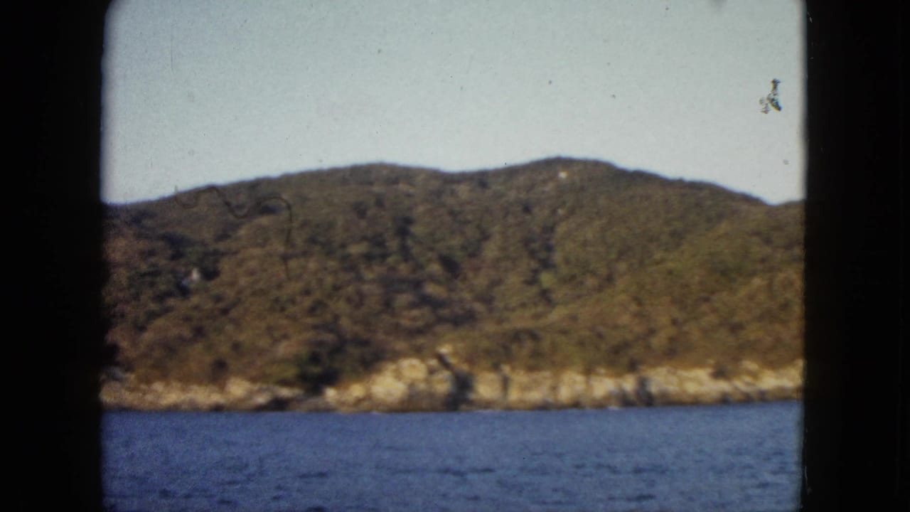 Acapulco coastline appears across blue water in a 1962 8mm travel frame with soft focus and visible gate edges.