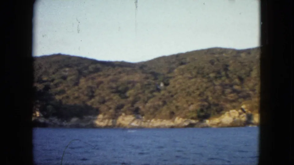 A later 1962 Acapulco frame shows open bay water, wooded hills, rocky shoreline, and faint film scratches.