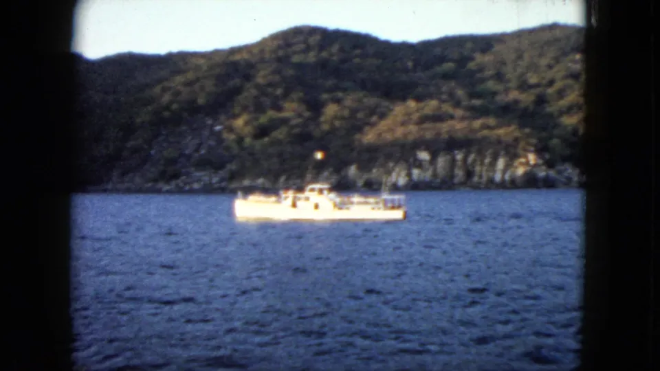 1962 Acapulco home-movie view of a small boat on open water with wooded hills and shoreline in the background.