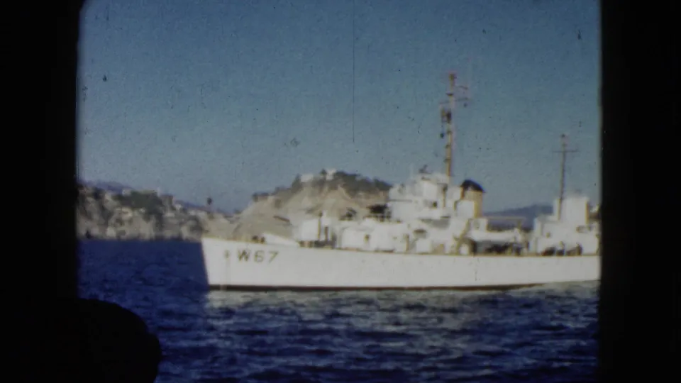 A white naval-looking vessel marked W67 passes off the Acapulco coast in 1962 home-movie footage, with cliffs and distant hills behind it.