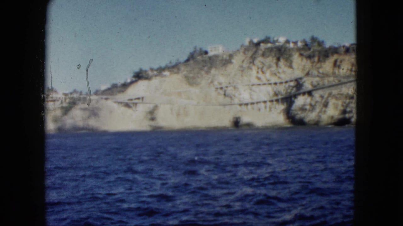 1962 Acapulco boat view showing blue ocean, pale cliffs, greenery, and small white buildings on the hillside.