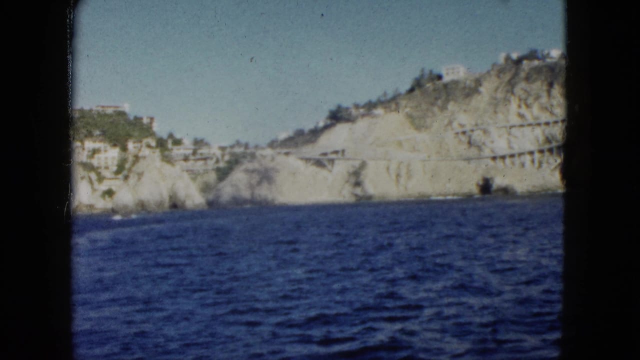 Blue ocean below a rocky cliff with white hillside buildings and a structure along the rock face.