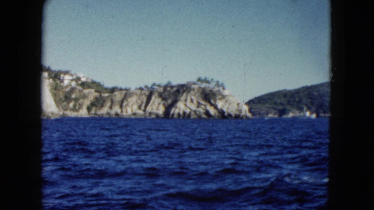 Deep blue water below rocky Acapulco coastline with hillside buildings and dark frame borders.