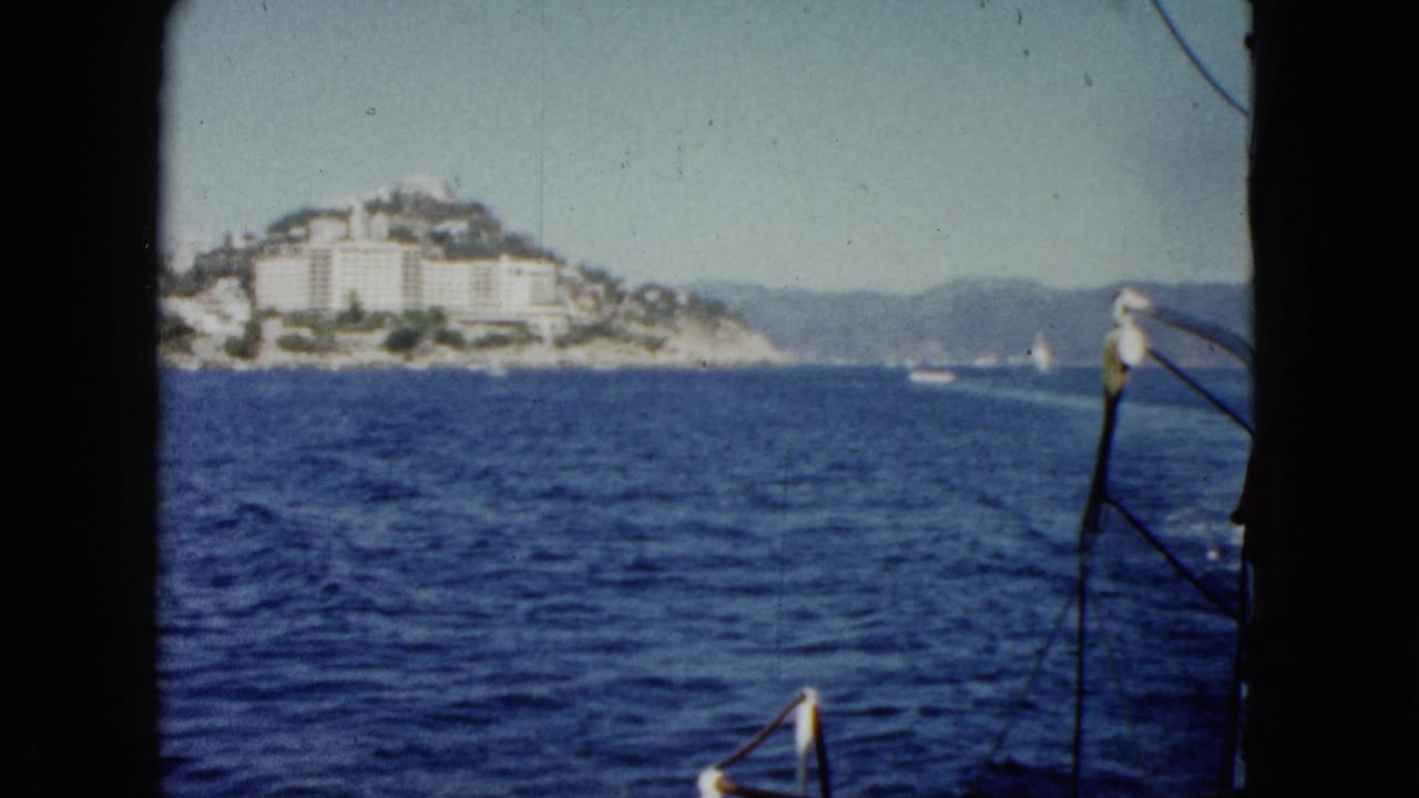 Boat-view coastline with blue water, distant hillside buildings, and dark film frame edges.