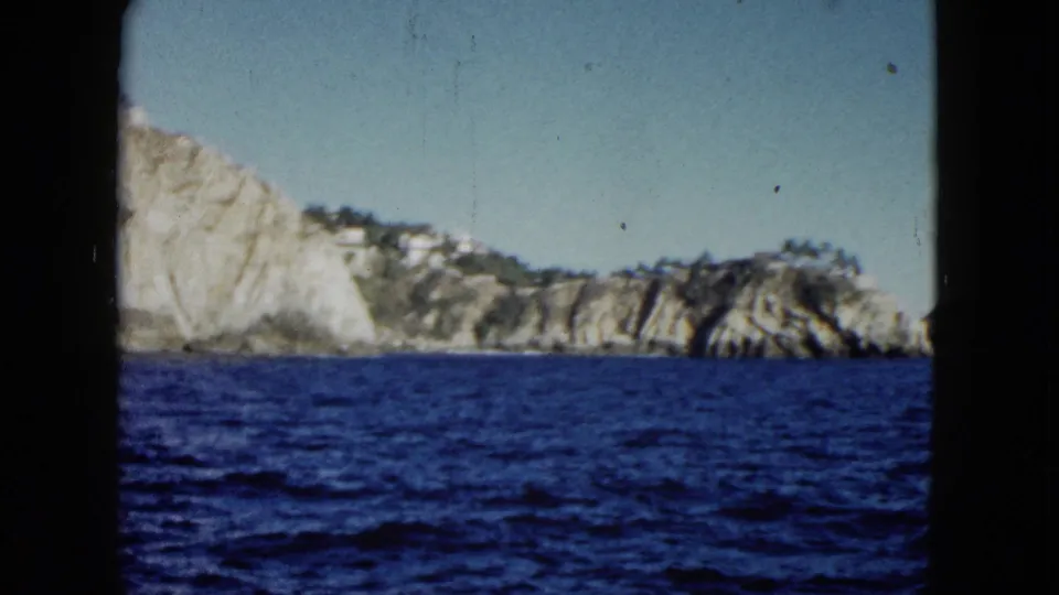1962 Acapulco 8mm frame showing rugged coastal rocks and vegetation from a passing boat.