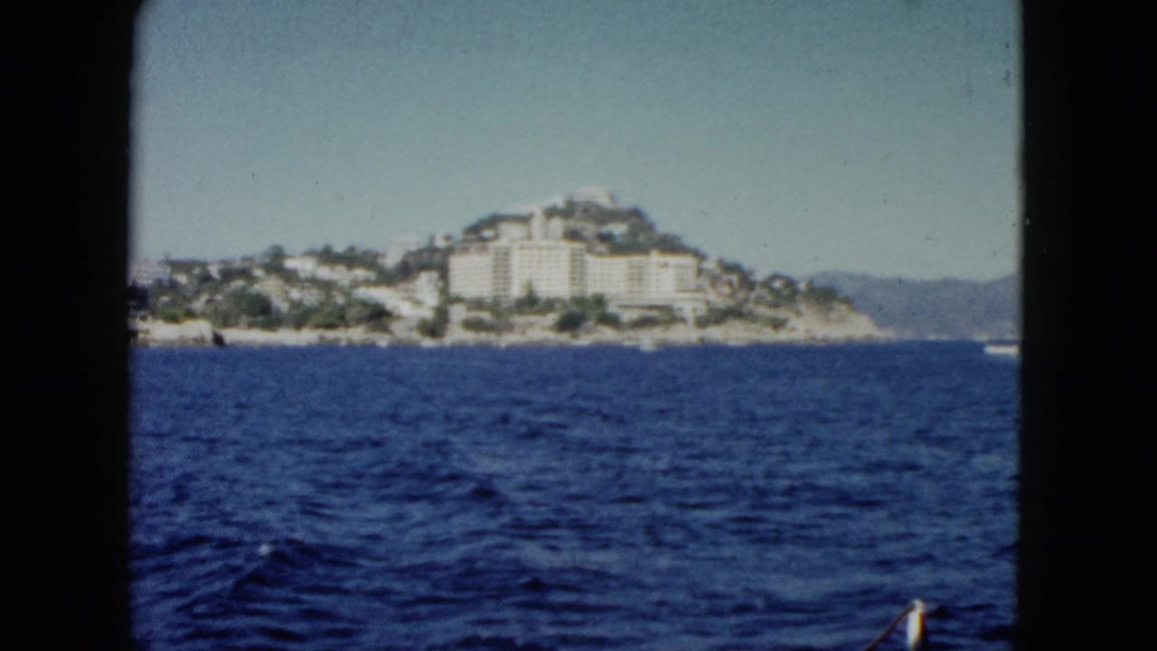 Distant coastal hillside and white buildings across open water, with dark vertical frame borders.