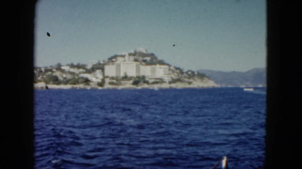 1962 Acapulco travel-film view across choppy blue water toward a hillside shoreline and distant mountains.