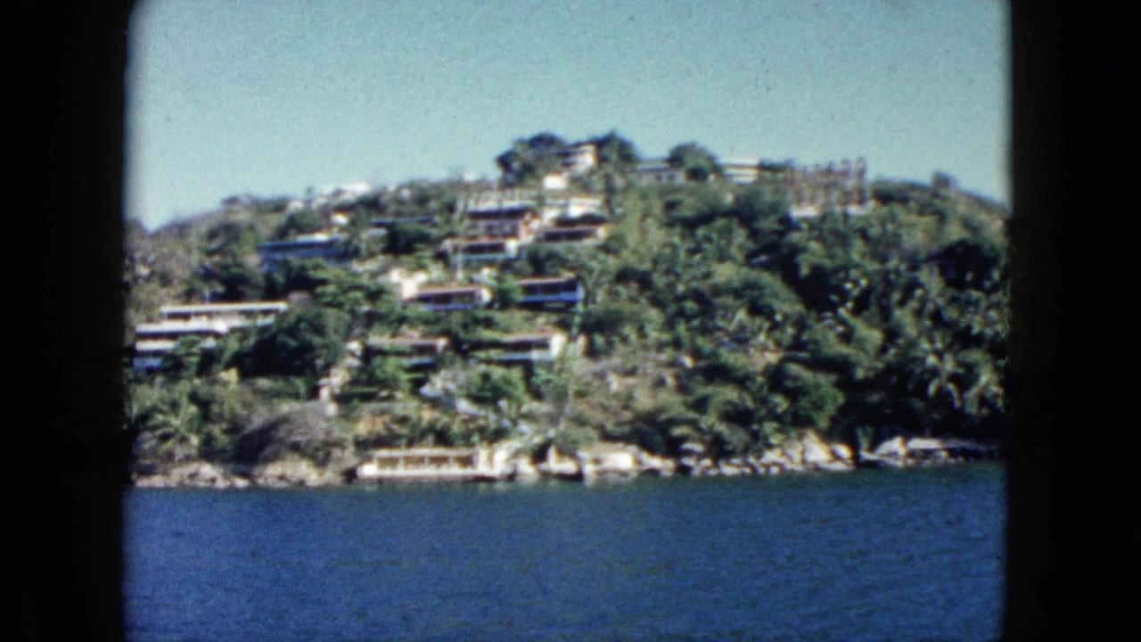 Green hillside with houses above blue water, seen from offshore.