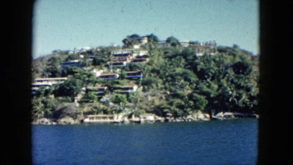 Wide 1962 Acapulco view of hillside resort buildings and vegetation overlooking the bay from a boat.