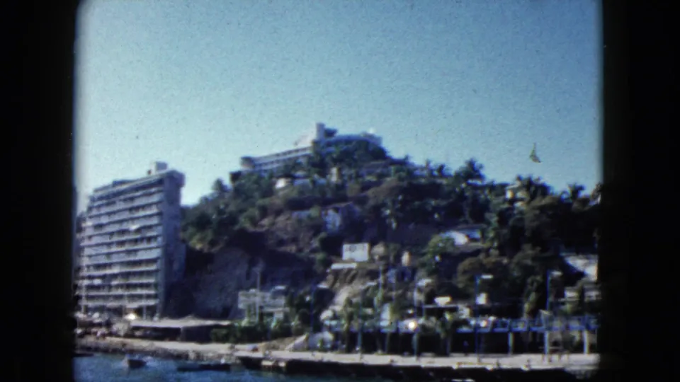 Acapulco, Mexico, 1962: modernist hillside hotel above a palm-lined harbor waterfront, shot on 8mm color film.