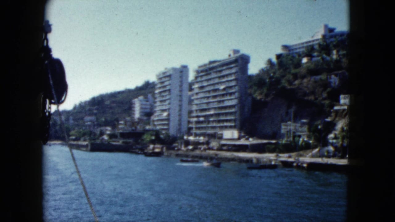 View from a boat across Acapulco Bay toward steep hillsides lined with multi-story resort hotels, circa 1962, 8mm home movie.