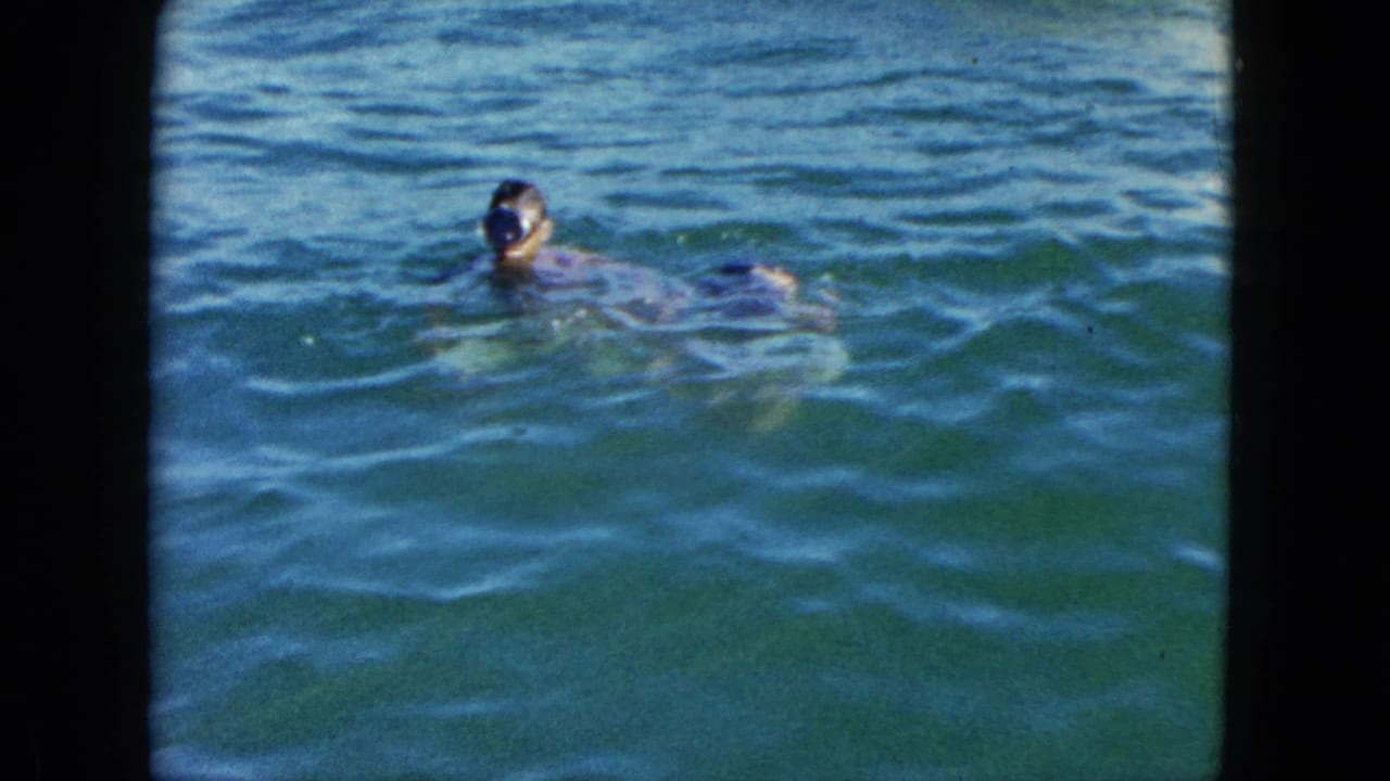 One child swimming in turquoise-green open water, head and shoulders visible above the surface.