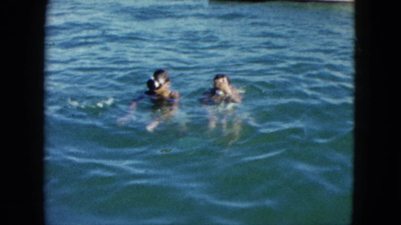 Two children swimming close together in turquoise open water, heads above the surface.