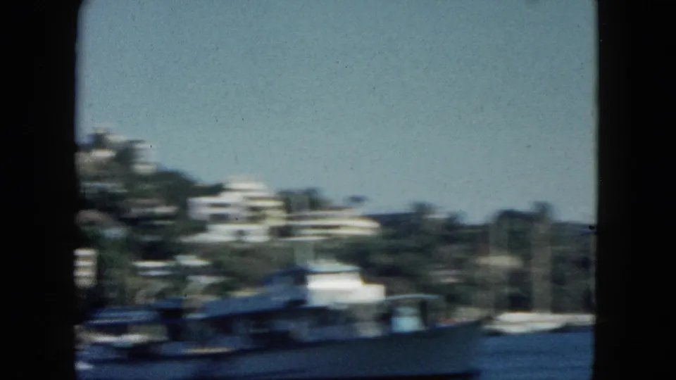 View from a moving boat across Acapulco bay, circa 1962 — motion-blurred white vessel in foreground, white structures on a densely vegetated hillside beyond.