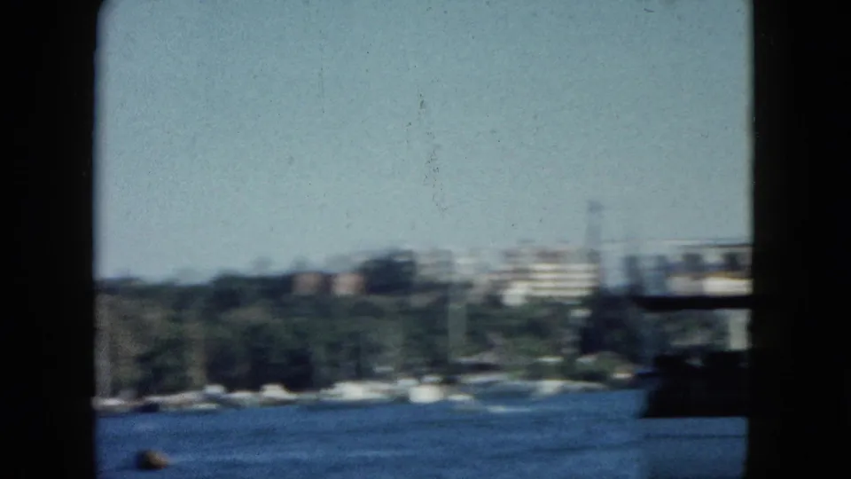 Wide pan across Acapulco harbour, circa 1962; wooded hills, coastal buildings, and open water visible with characteristic 8mm motion blur.