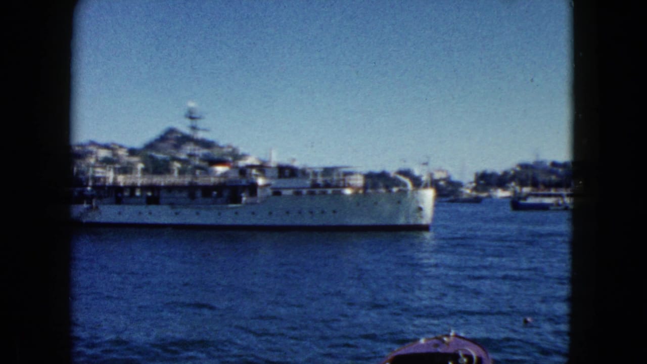 Naval vessel mid-transit through Acapulco harbor, 1962, showing superstructure and radar mast; hillside with buildings in background.