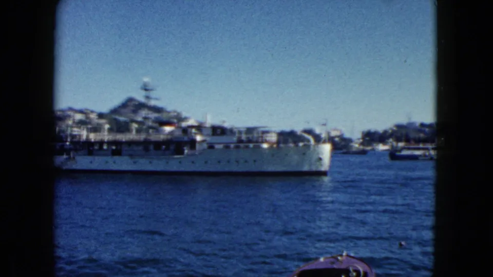 Naval vessel mid-transit through Acapulco harbor, 1962, showing superstructure and radar mast; hillside with buildings in background.