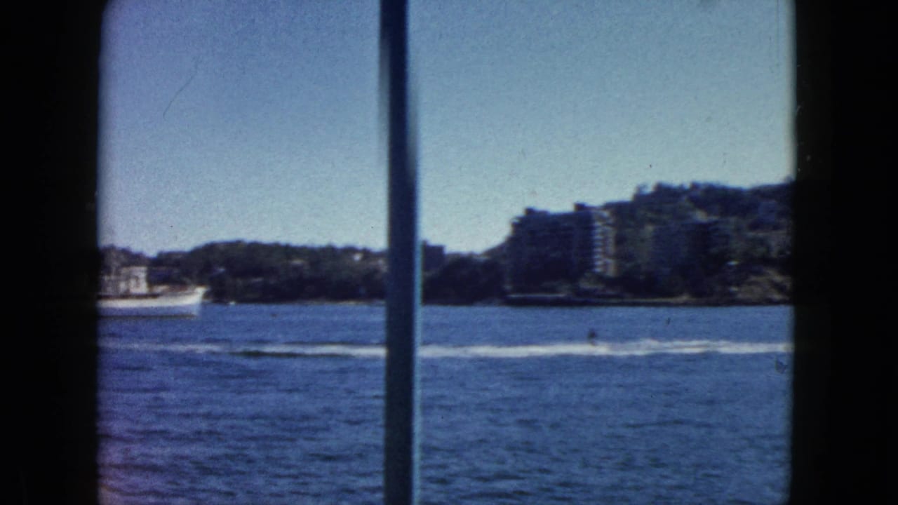 8mm home movie frame c.1962 showing Acapulco harbour: white passenger ship at mid-distance, forested hillside, and multi-storey buildings on the opposite shore.