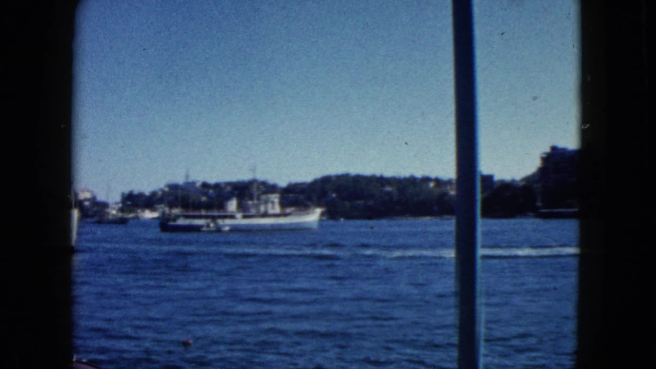8mm travel footage c.1962, Acapulco harbour: large white ship at centre, cylindrical or domed white shore structure, tree-lined hillside, mid-century buildings.
