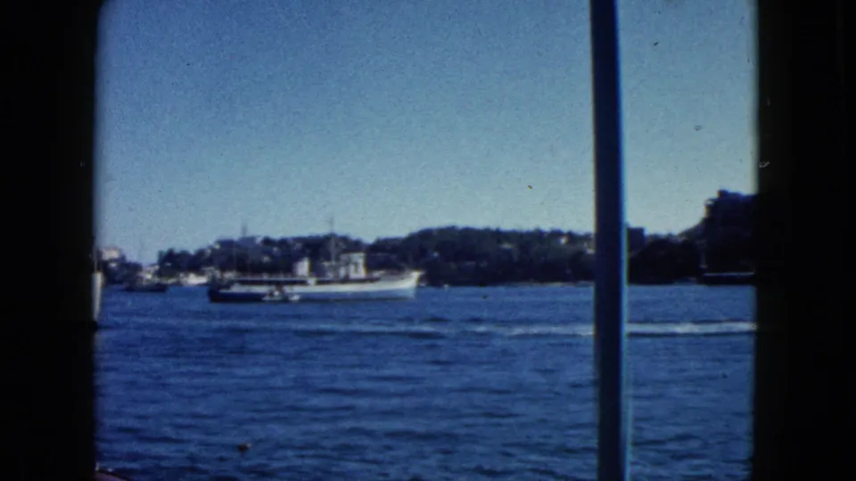 8mm travel footage c.1962, Acapulco harbour: large white ship at centre, cylindrical or domed white shore structure, tree-lined hillside, mid-century buildings.