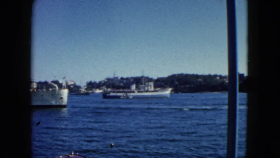 8mm home movie c.1962 showing at least two harbour vessels — a white ship port side and a larger mid-harbour vessel — with Acapulco's tree-lined shoreline behind.