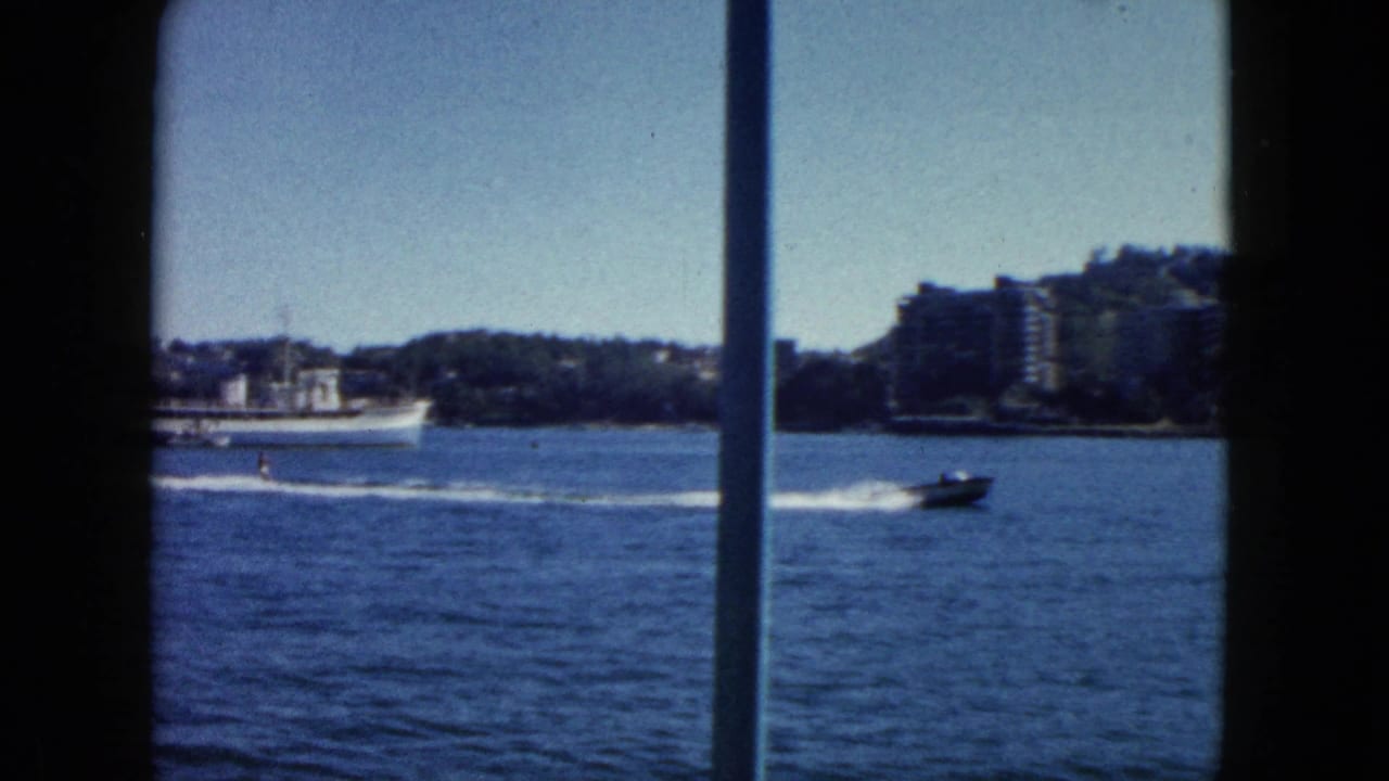 8mm footage of Acapulco bay circa 1962; large white ship at centre, speedboat crossing right with white wake, early resort buildings on hillside.