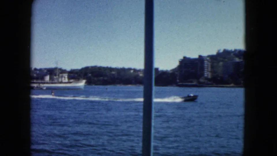 8mm footage of Acapulco bay circa 1962; large white ship at centre, speedboat crossing right with white wake, early resort buildings on hillside.