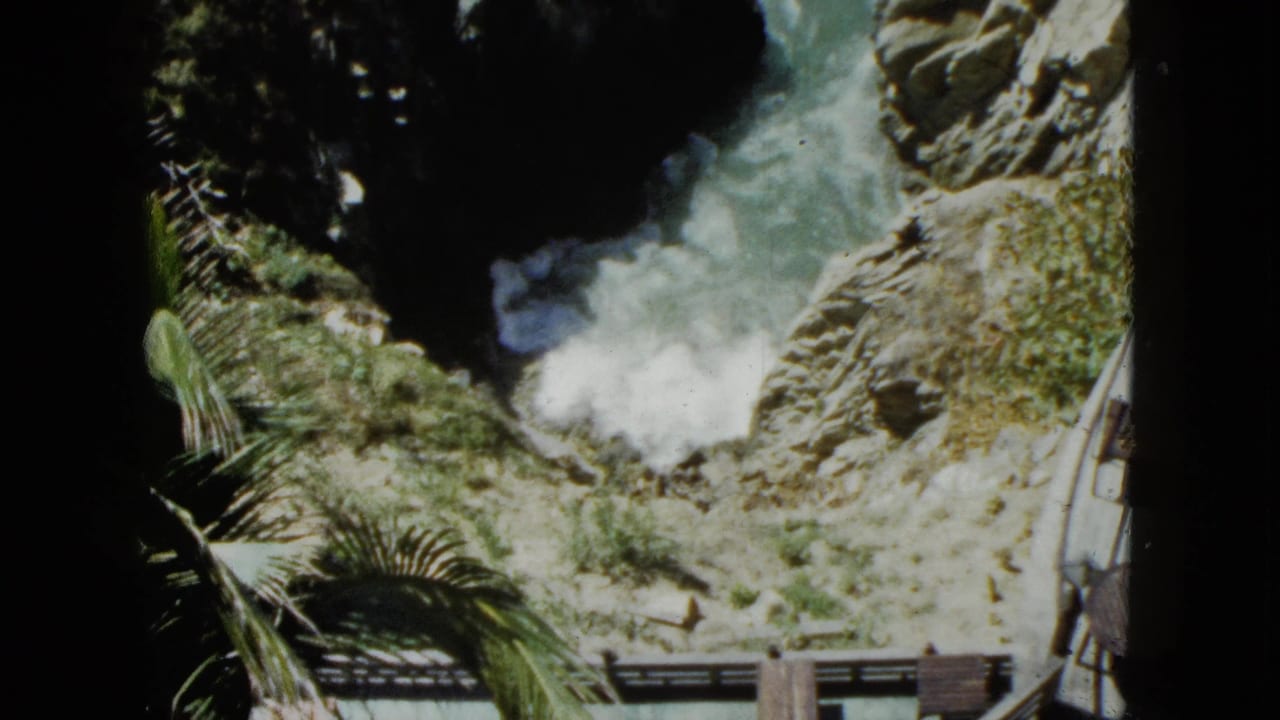 Overhead shot from a scenic overlook showing a rocky coastal cove in Acapulco, Mexico, circa 1962; turquoise waves surge between dark rock faces.