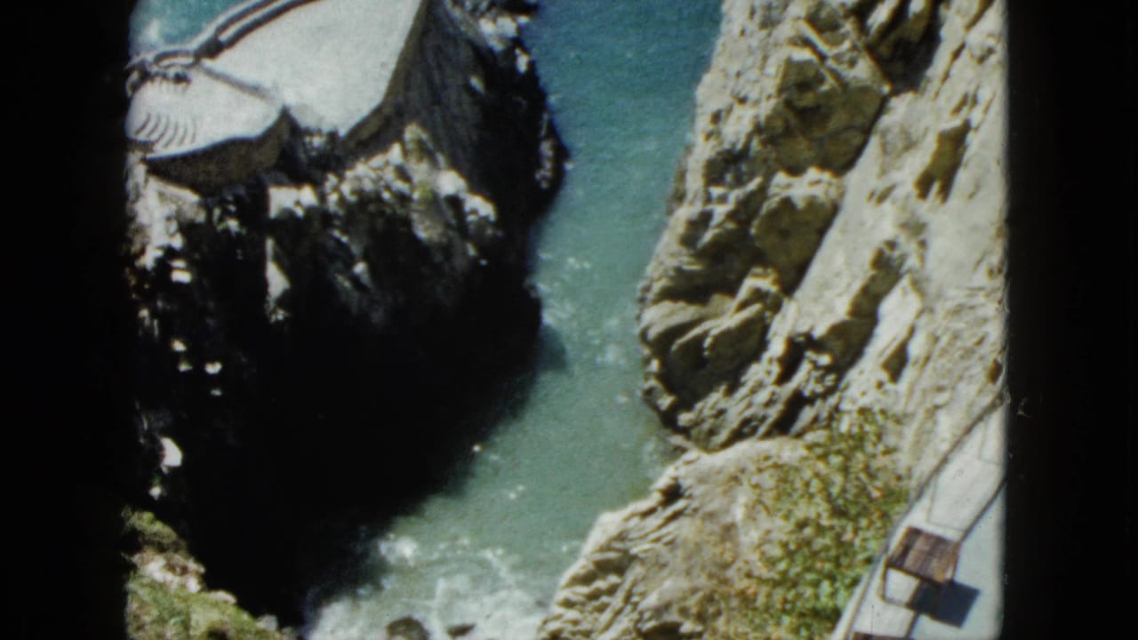 Steep rocky cliffs with a narrow turquoise cove below, photographed looking almost straight down from a clifftop vantage.