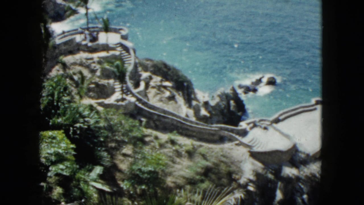 8mm pan showing stone cliff walkway curving around rocky headland above turquoise water, Acapulco, 1962.