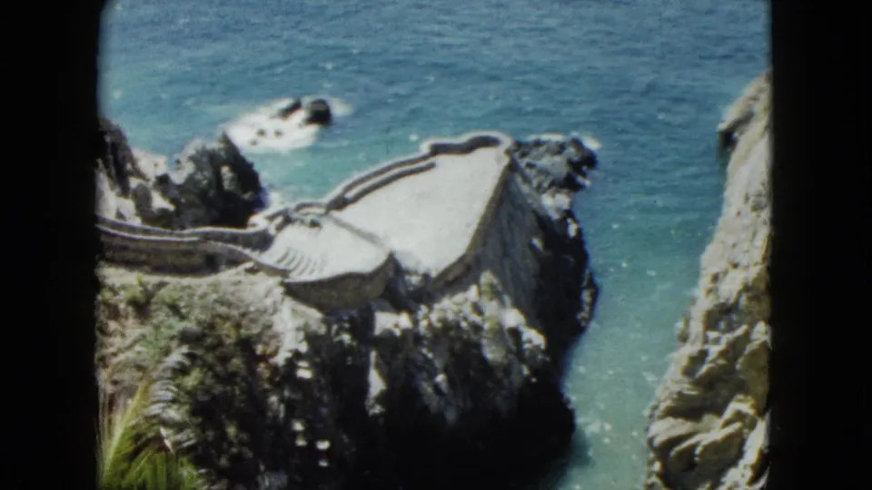 8mm home movie final frame showing stone cliff staircase and terraced walkway at Acapulco, Mexico, circa 1962, with turquoise Pacific visible below and rocky cliff edge at right.