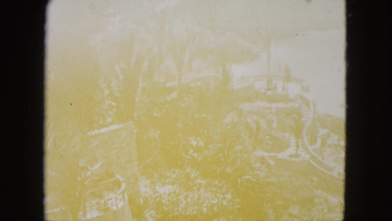 Faded opening frame from 1962 Acapulco footage, with the rocky coast and palm-lined overlook barely visible through heavy exposure bloom.