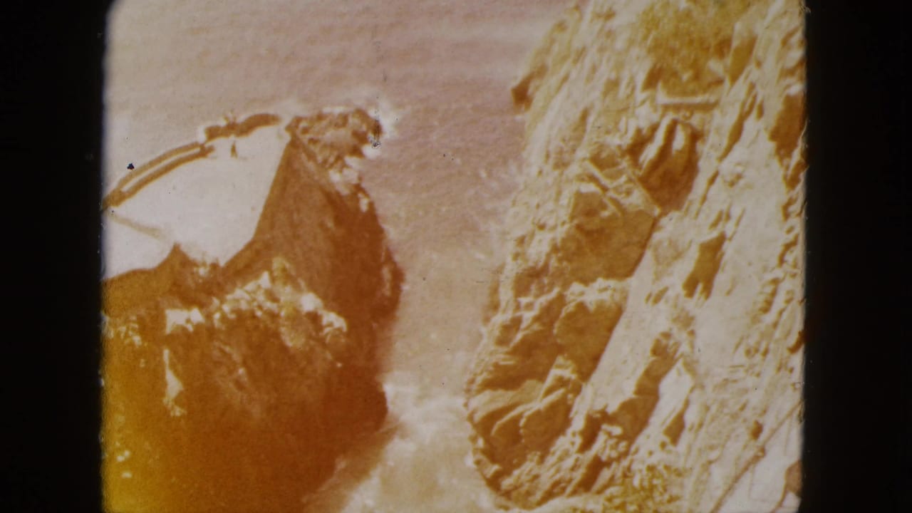 Close-up of rugged cliff terrain, likely in the Acapulco, Mexico area, circa 1962, showing amber dye shift and coarse grain characteristic of 8mm home movie film.