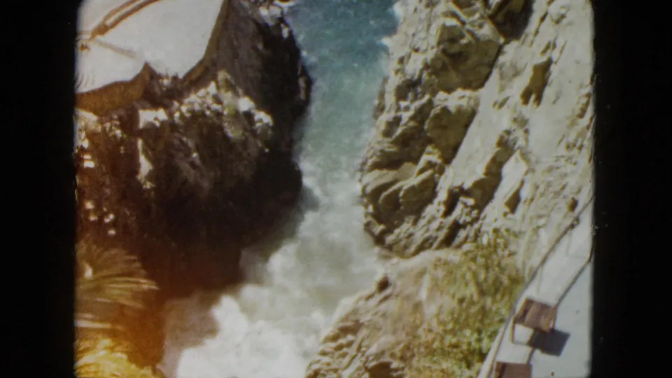 8mm frame from Acapulco, 1962, showing the rocky cliff and coastal terrace railing; a warm orange cast at the left edge signals onset of photochemical color degradation in the film stock