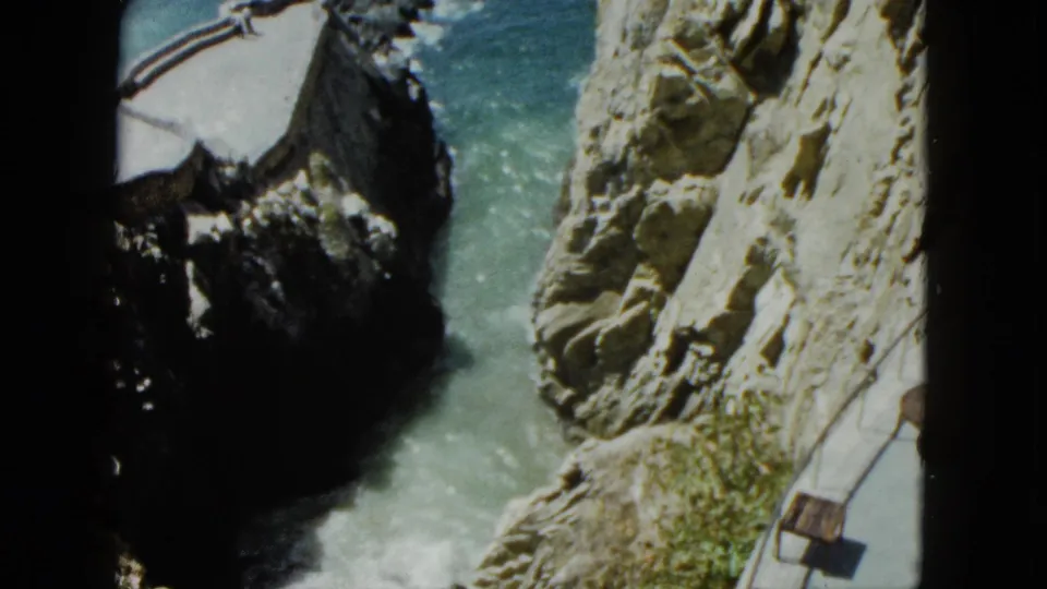 8mm home movie from Acapulco, 1962: cliff and Pacific surf with foreground railing suggesting filming from a tourist viewpoint or elevated platform.