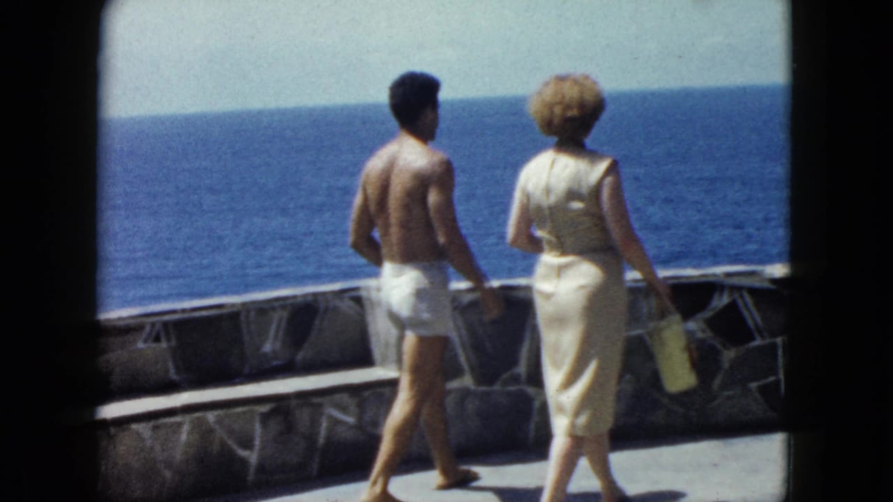 Couple walking away along a stone-walled ocean terrace, deep blue sea beyond, Acapulco area, circa 1962, 8mm color home movie.