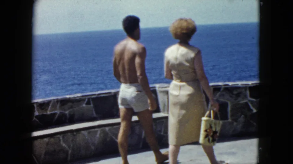 Couple on stone coastal terrace with ocean panorama, woman with patterned beach bag, Acapulco, circa 1962, 8mm film.