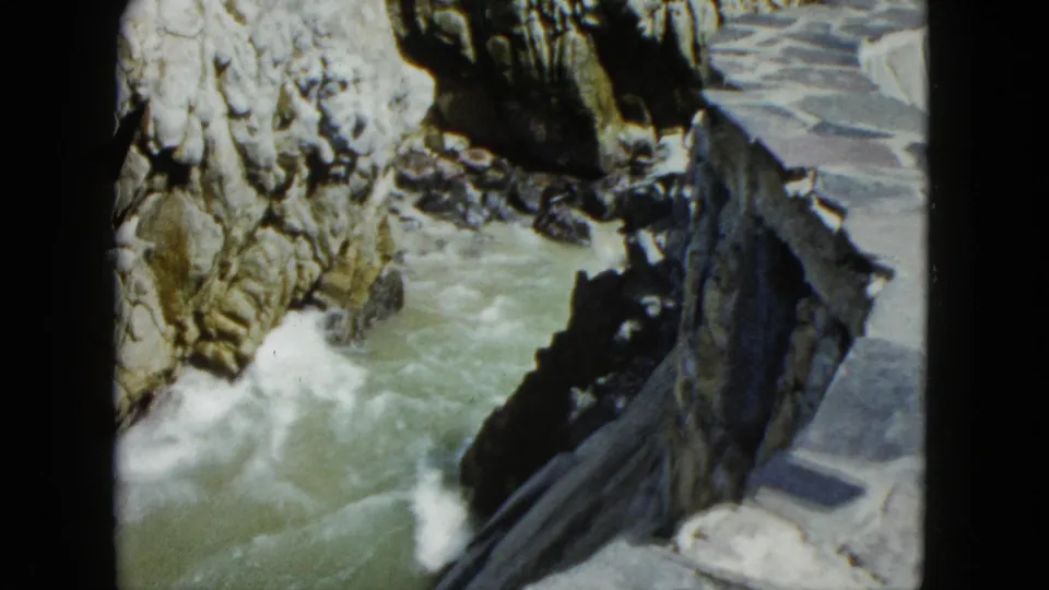 8mm frame showing coastal rocky cliffs with crashing white foam and a stone path at lower right, Acapulco area, circa 1962.