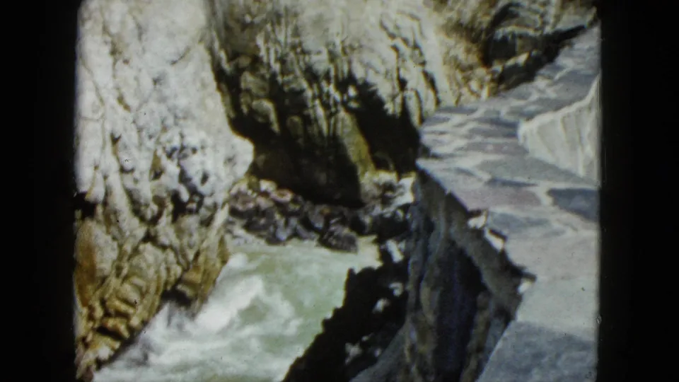 8mm home movie frame of rugged rocky cliff face with rushing water below, likely Acapulco coastal canyon, circa 1962.