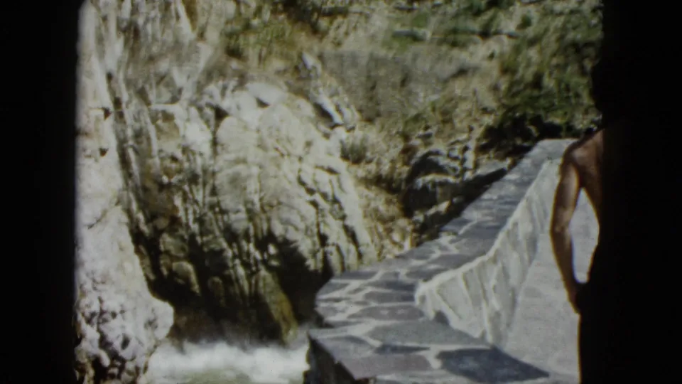 8mm frame of a stone path with a partial figure in swimwear at right edge overlooking a rocky canyon, Acapulco, circa 1962.