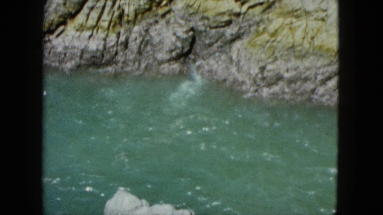 Green-blue river water below layered rock, seen through dark 8mm frame edges.