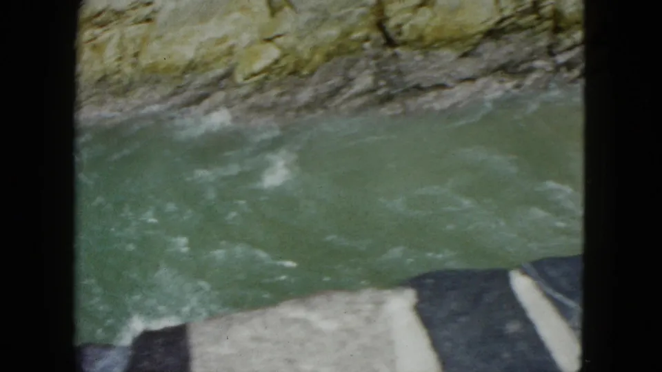 1962 Acapulco home-movie view of a rocky river channel with green water, white foam, and partial dark film or foreground edge.