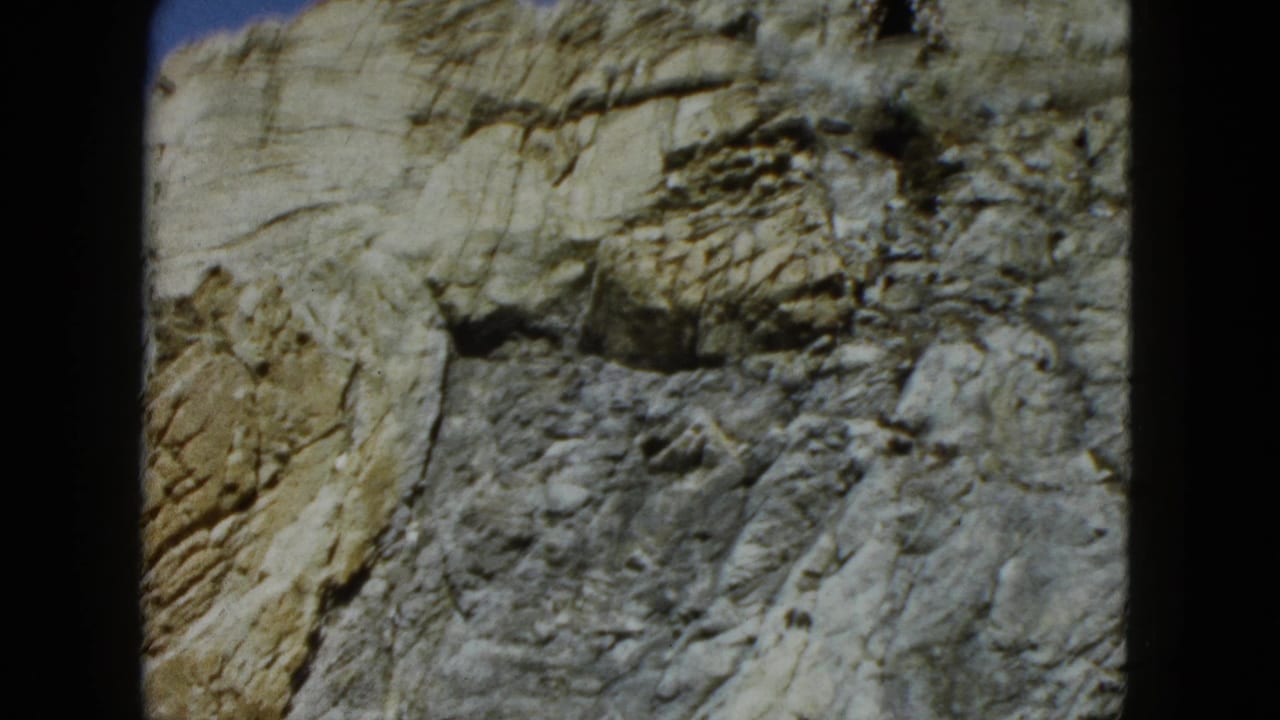 Sunlit craggy rock face framed by dark 8mm film borders.