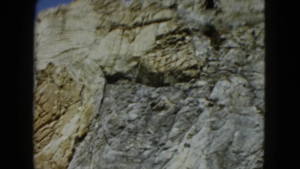 1962 Acapulco 8mm frame showing a pale, craggy coastal rock surface in close view with dark film borders.