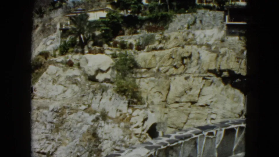 8mm film frame showing a limestone cliff face identified as Acapulco, Mexico, circa 1962, with resort-style buildings and palm trees at the crest.