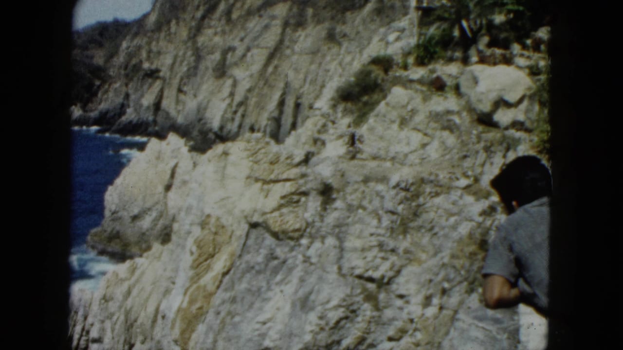 Tourist-era man at coastal cliff edge, Acapulco-area white limestone cliffs and deep blue Pacific beyond, 8mm home movie circa 1962