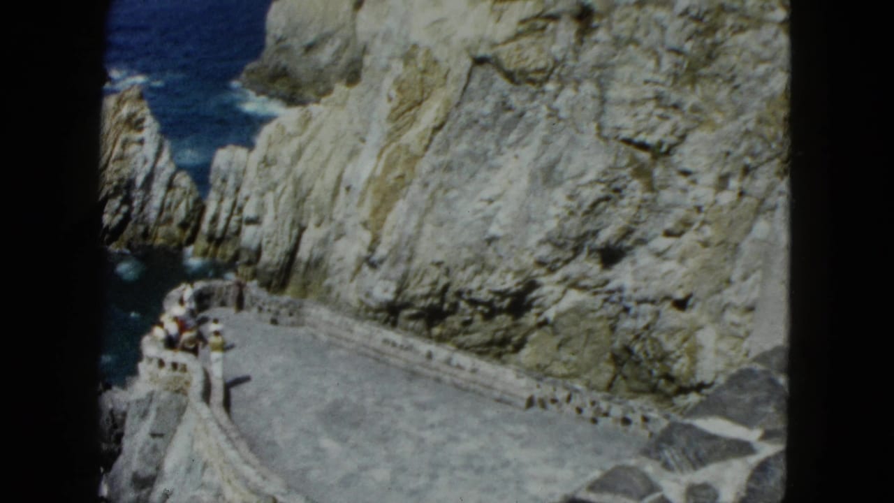 Stone walkway curves to a rounded observation point on a cliff, small group of visitors at far end, ocean below.