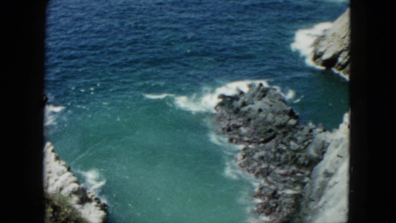 Rocky coastal cove with blue-green water and surf washing against jagged rocks.