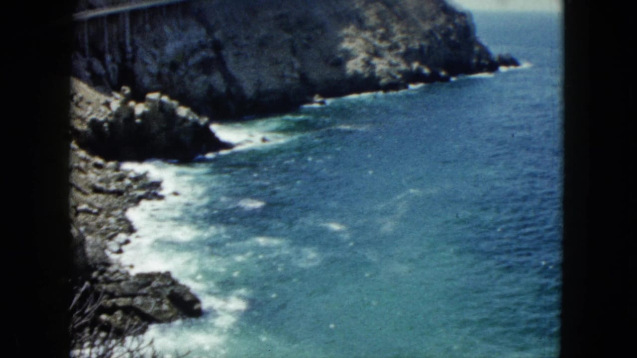 Elevated view of a rocky coastline with turquoise sea and white surf breaking against rocks, shot on 8mm color film.