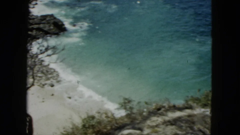 Small sandy cove with turquoise water seen from an elevated position in 8mm color footage reportedly from Acapulco, Mexico, 1962.